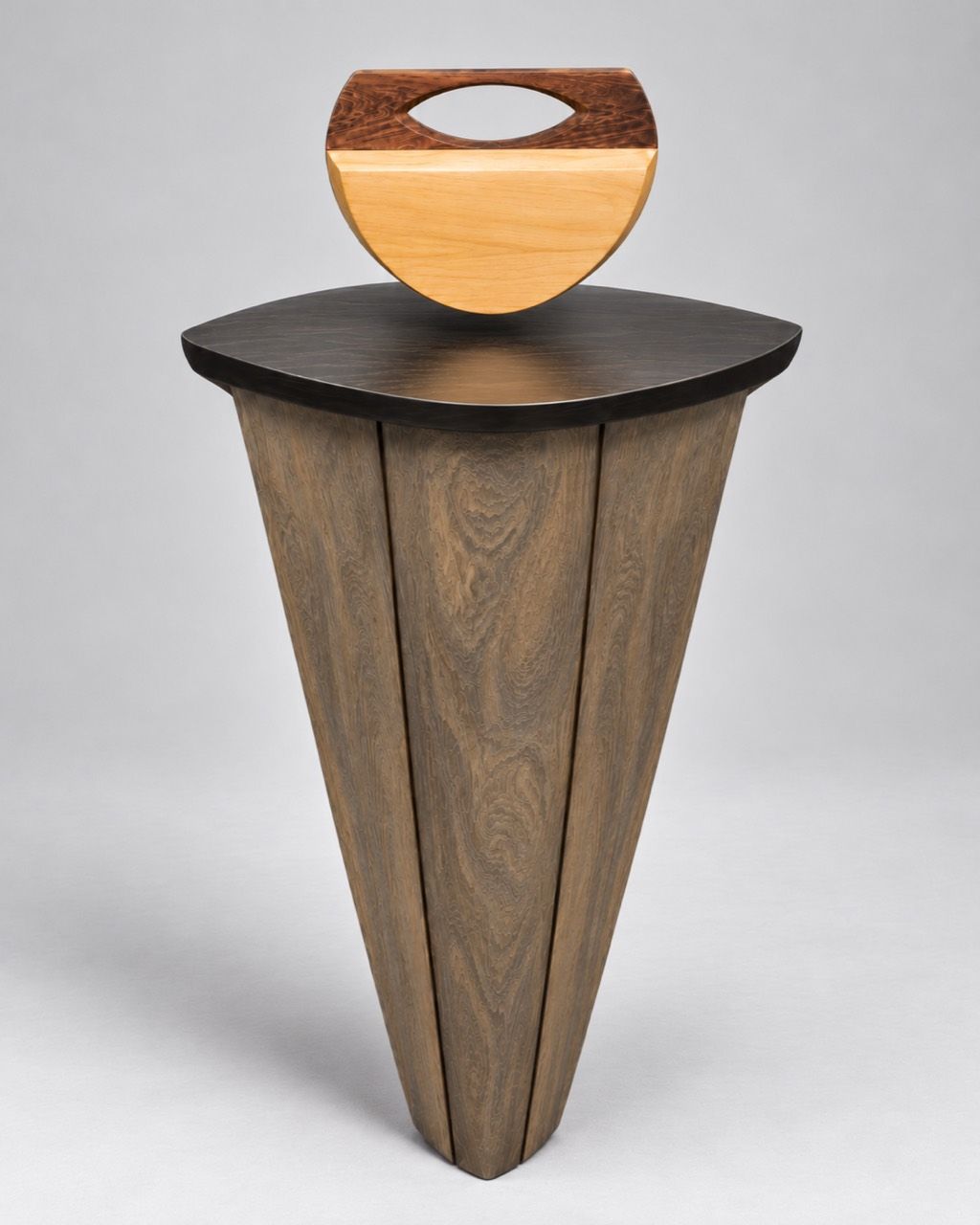 Culla d'Ombra, a half-round pale wooden handbag with a dark figured cap, resting on a tall wooden pedestal